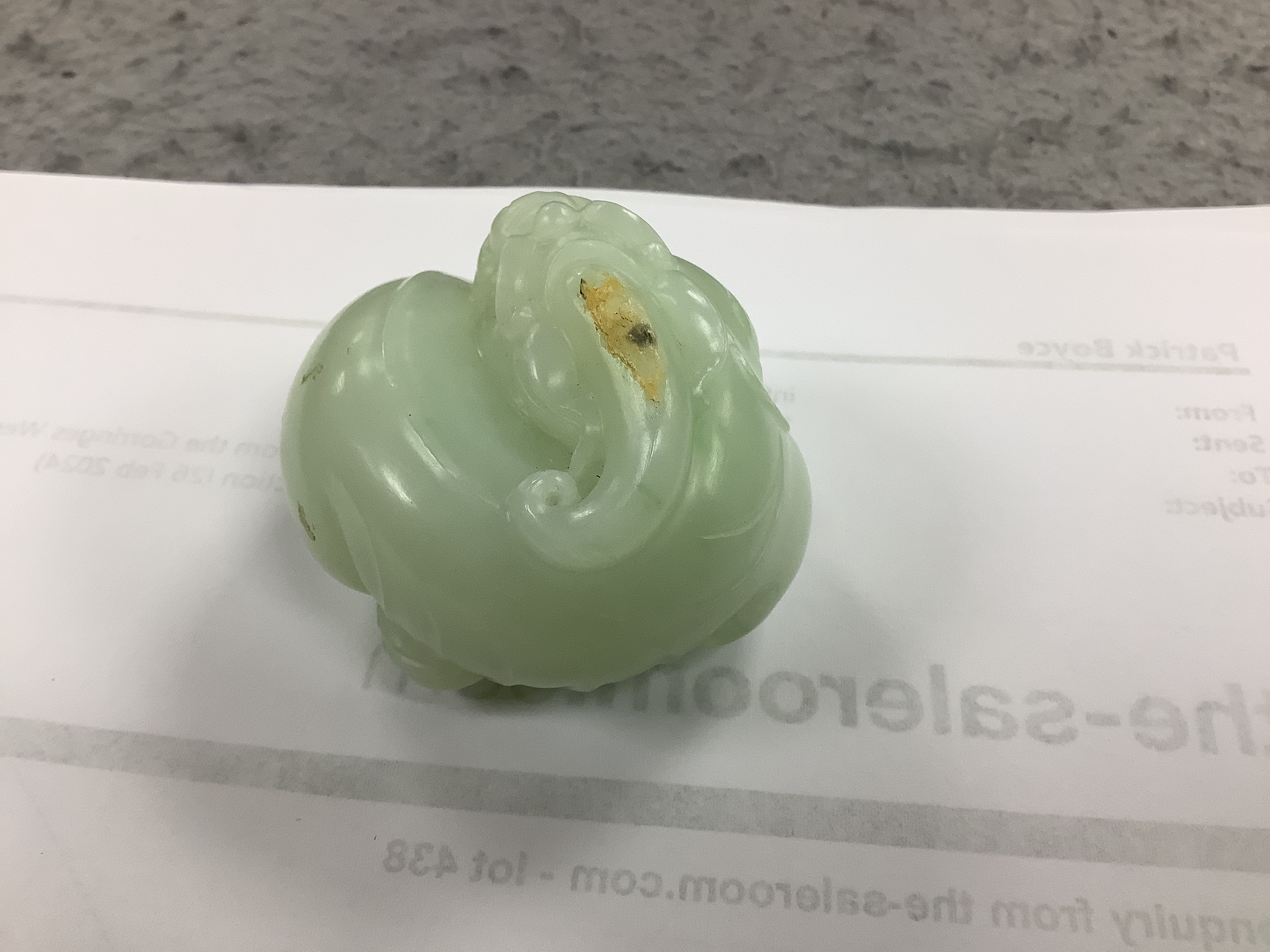 A Chinese celadon jade carving of a lion-dog, in recumbent pose, its crest with a russet inclusion, 5.3cm